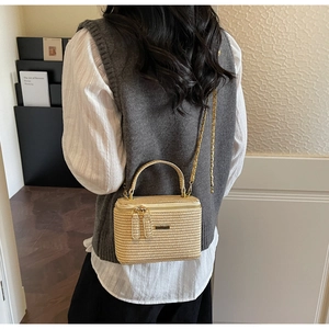 Detail of woven straw box bag featuring dual zippers and elegant gold chain strap