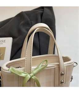 Detail of beige plaid bucket bag with a green satin bow and metallic rivets