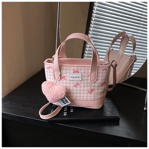 Pink bucket bag detail with checkered canvas, bow print, and heart-shaped plush charm