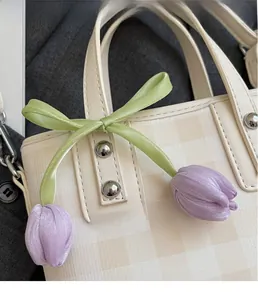 Detailed close-up of a purple silk tulip charm with green bow on a checkered handbag