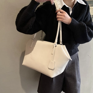 Detail of a minimalist cream white tote bag in lychee pattern leather with a square pendant