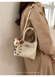 Dettaglio borsa a secchiello in pelle beige con ciondolo orso e tracolla di perle