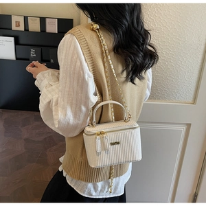 Detail of white woven texture on crossbody bag with gold chain and metal logo plate