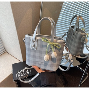 Détail du sac seau à carreaux gris avec breloque tulipe et bandoulière sur un livre