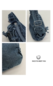 Detail of blue denim crossbody bag featuring fringe zippers and silver metal hardware