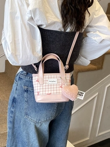 Pink checkered bucket bag with heart charm shown on a person for size perspective