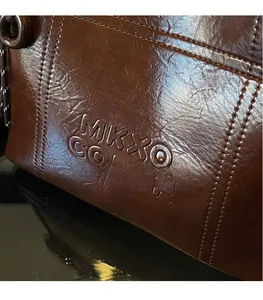 Macro shot of dark brown oil wax leather tote featuring embossed logo and fine stitching