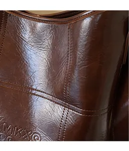 Detail of dark brown leather tote bag with crinkled texture and MKXO logo embossing