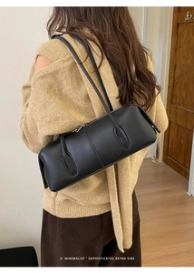 Minimalist black retro baguette bag shown on shoulder in cozy indoor setting
