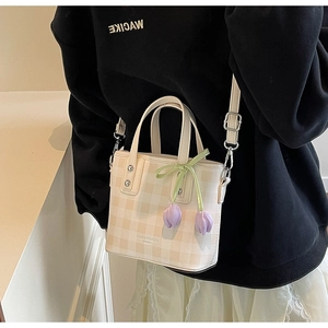 Detailed view of cream checkered bucket bag with tulip charm and adjustable strap