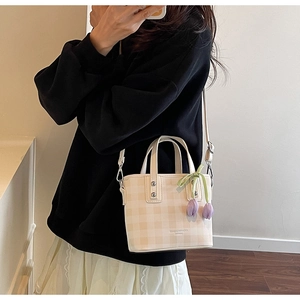 Detailed view of checkered bucket bag with flower charm held by model in casual outfit