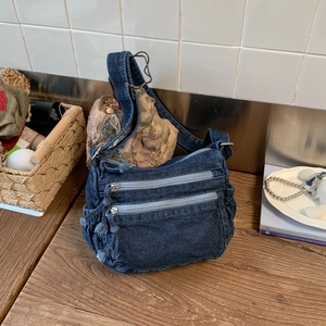 Detail view of denim shoulder bag with metal buckles and double zip pockets