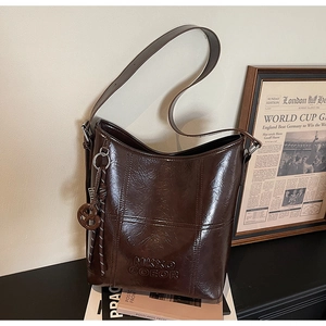 Detailed shot of dark brown oil wax leather bucket bag with embossed logo on table