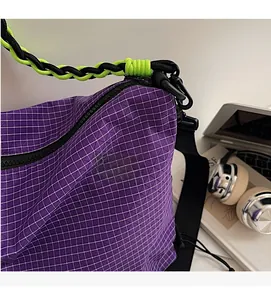 Close-up of purple plaid nylon crossbody bag with green braided rope strap detail