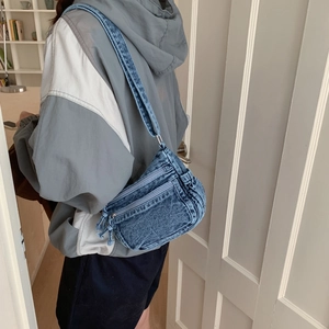 Detail of blue denim crossbody bag with multiple zippers shown on a lifestyle model
