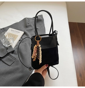 Close-up of black suede bucket bag featuring artistic wooden bead charm and metal magnetic snap
