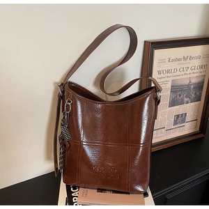 Detail of dark brown bucket bag with embossed logo, contrast stitching and chain link strap