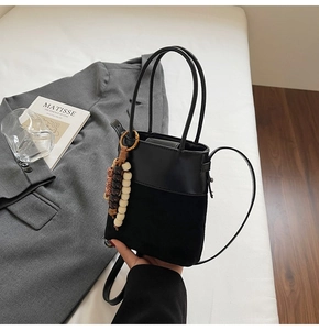 Detail of black suede and leather bucket bag with decorative wooden beads on a white bed