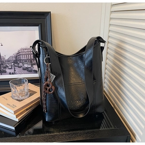 Close-up of black bucket bag with MKXO logo and stylish braided cord pendant charm