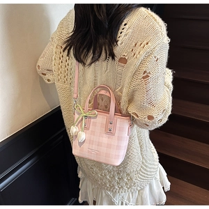 Détail du sac seau à carreaux roses avec nœud vert et breloque tulipe sur un escalier