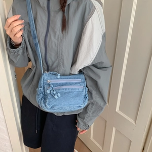 Detailed view of light blue denim crossbody bag with retro frayed edges and zippers