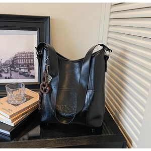 Detail of black oil-wax leather bucket bag with MKX COCO logo and bow charm decoration