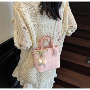 Detail of pink plaid handbag featuring tulip pendants and a green ribbon charm