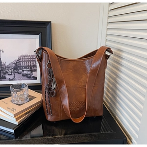 Detail of vintage brown bucket bag with tassel charm and embossed logo on glossy leather