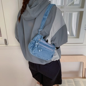 Detail view of denim crossbody bag with multiple zip pockets and adjustable strap