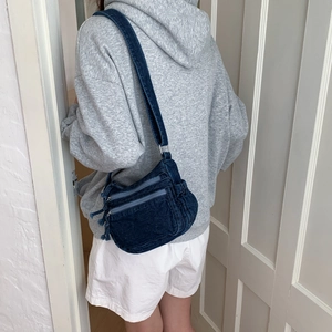 Detail of blue denim crossbody bag featuring multiple zipper pockets and adjustable strap