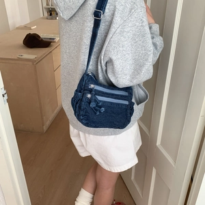 Detailed view of dark blue denim crossbody bag featuring layered zippers and adjustable strap