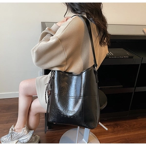 Detail of black textured bucket bag with embossed MKXO letters and tassel pendant decor