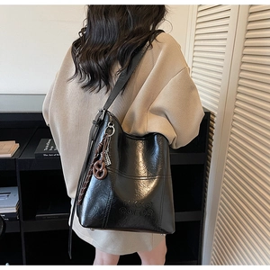 Detail of black leather bucket bag featuring MKXG COLOR embossed logo and pretzel charm