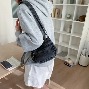 Detailed view of black denim crossbody bag featuring multiple zipper pockets and washed texture