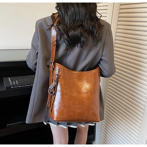 Close-up of caramel leather bucket bag texture and embossed logo with adjustable strap