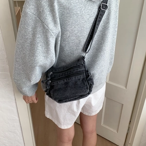 Detail of vintage denim crossbody bag with multi-zipper layers and adjustable strap