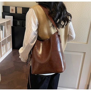 Detail of a brown quilted leather bucket bag with embossed logo and long shoulder strap