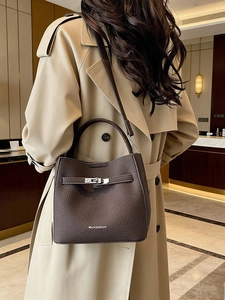 Dark brown leather bucket bag with top handle and metal lock worn with khaki trench coat