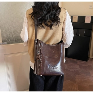 Detail of dark brown glossy leather bucket bag with embossed logo and braided knot charm
