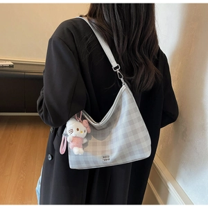 Détail du sac à carreaux gris avec zip argenté et breloque en peluche sur un blazer noir