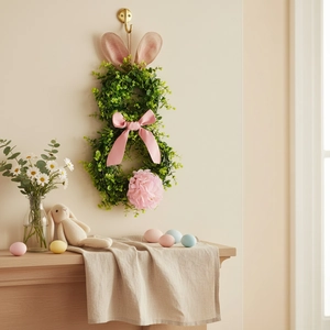 Close-up of Easter bunny wreath with green foliage, pink ears, and silk bow on a wall