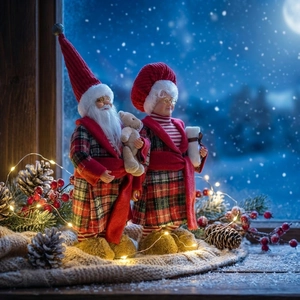 Standing Santa and Mrs. Claus plush figures in red and green plaid robes on a cozy window