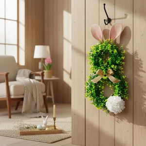 Easter bunny wreath with green foliage, pink ears and golden bow on wooden wall