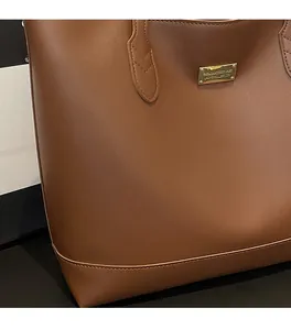 Detail of premium brown leather tote bag with gold metal plate and stitching