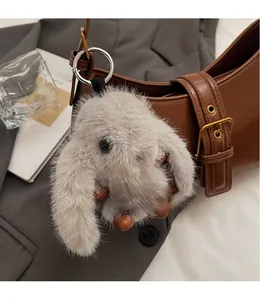 Detail of a fluffy grey bunny plush keychain hanging on a brown leather bag strap