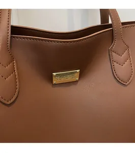Close-up of golden metal plaque and fine stitching on a premium brown leather tote bag