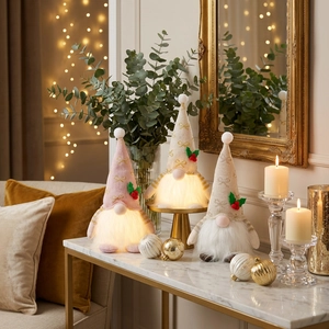 Tre gnomi di Natale luminosi con cappelli di paillettes dorate e luci LED su tavolo marmo