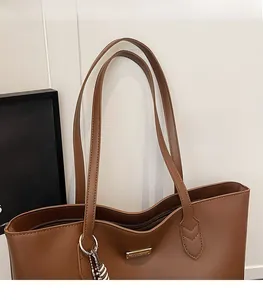 Detail of a brown faux leather tote bag with thin double shoulder straps and golden logo