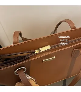 Close-up of smooth gold metal zipper and brand plate on brown leather tote bag