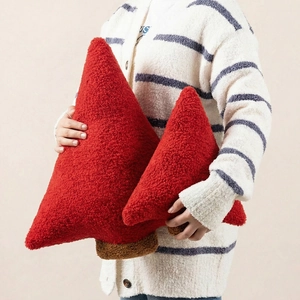 Detail of red Christmas tree plush pillows in soft sherpa fabric held by a model